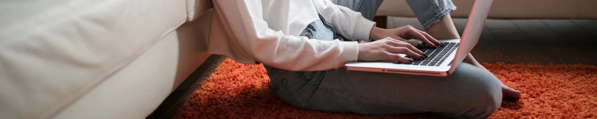 Woman using a laptop while sitting on an orange area rug